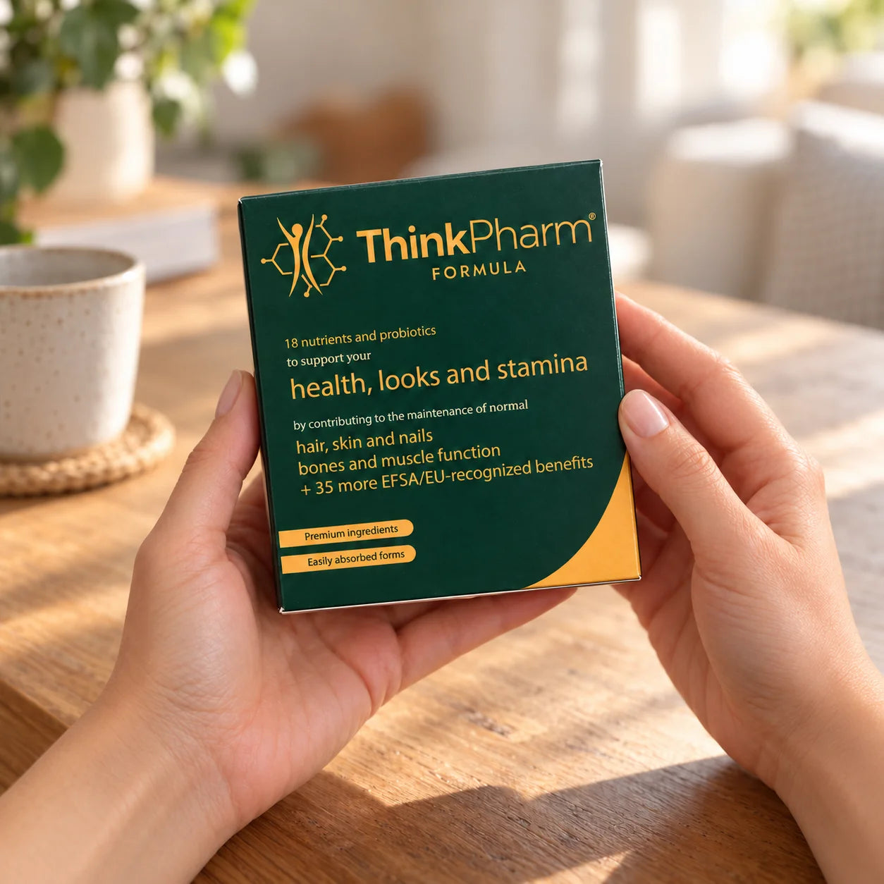 Woman’s hands holding the ThinkPharm Formula pack over a wooden table in soft daylight.